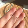 A pair of pearl flower stud earrings being worn on a person's hand, with various other jewelry items in the background.